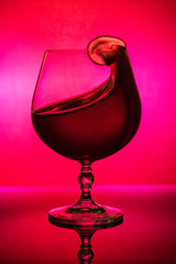 Splash of red wine to the edge of a glass goblet, on a red background with a gradient spot