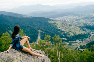Lonely young traveler girl siiting on stone at top of mountain. Discovering new country. Beautiful nature landscape from high altitude. Summer trip on weekend vacation.  Edge of world. Jeans clothes.