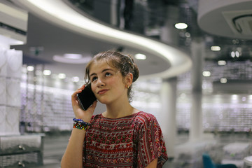 Young blond cute girl talking on a mobile phone and thinking while looking in the distance