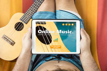 Young man lying on a hammock visiting an online music website with tablet device
