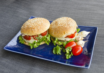 Two vegetarian beluga lentils and hemp seed burgers, stacked with homegrown salad, onion rings, tomatoes, in homemade rye buns with sesame seeds.