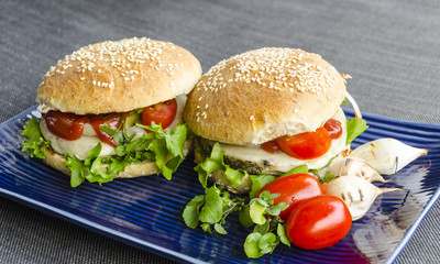 Healthy fast food with two beluga lentils and hemp seed burgers, stacked with homegrown salad, onion rings, tomatoes, in homemade rye buns with sesame seeds.