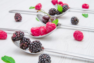 Fresh berries on steel spoons on white marble background