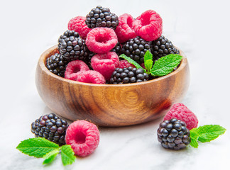 Wooden cup with fresh berries on white marble background