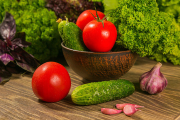 Tomatoes, garlic bulb and cucumbers on a wooden table. Green salad in the background.