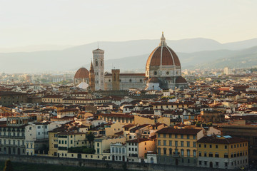 Elevated look at Florence city downtown dominated by Santa Maria Del Fiore cathedral with mountains in the background with sunset light