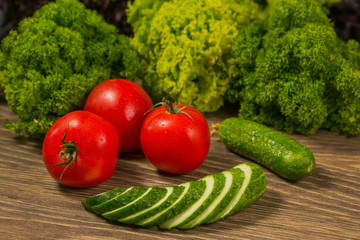 Помидоры и огурцы на старом деревянном столе. Листья салата и петрушка на заднем плане. Концепция здорового питания