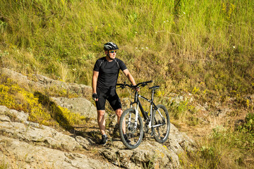 Obraz premium Mountain biker with a bicycle on a rock. Motivation and inspiration for adventure.