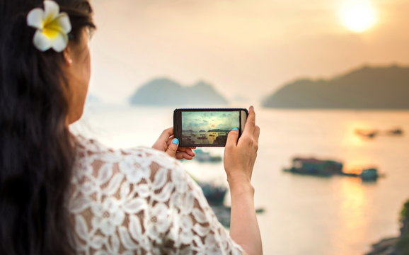 Girl taking seaside sunset picture with smartphone