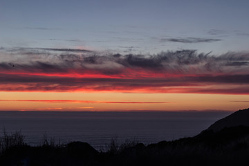 Shot of the Atlantic Ocean, with red sunset clouds, and the silhouette of the cliffs in Finisterre, Galicia, Spain