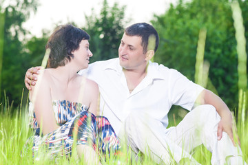 Family Relationships. Happy Caucasian Couple Relaxing Together Outdoors on Grass in Park. Sitting Embraced and Looking at Each Other.