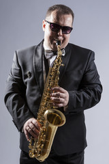 Naklejka premium Music Concepts. High Contrast Portrait of Caucasian Mature Expressive Saxophone Player Posing in Suit Against White Background.