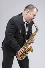 Fototapeta na wymiar Music Concepts. Portrait of Caucasian Mature Expressive Saxophone Player Posing in Suit Against White Background