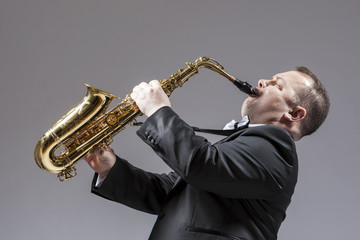 Fototapeta na wymiar Music Concepts. Full Length Portrait of Caucasian Mature Expressive Saxophone Player Playing the Instrument Against White Background.
