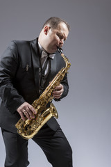 Fototapeta na wymiar Music and Musicians Ideas and Concepts. Portrait of Caucasian Mature Expressive Saxophone Player Playing the Instrument Against White Background.