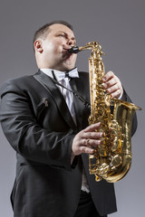 Fototapeta premium Music and Musicians Ideas and Concepts. Portrait of Caucasian Mature Expressive Saxophone Player Playing the Instrument Against White Background.