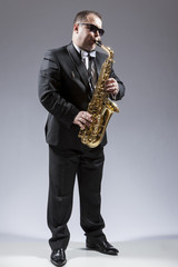 Music and Musicians Ideas and Concepts. Full Length Portrait of Caucasian Mature Saxophone Player in Sunglasses Playing the Instrument Against White.