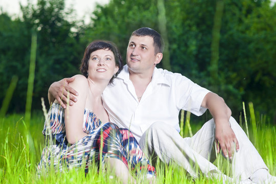 Family Relationships. Happy Caucasian Couple Relaxing Together Outdoors on Grass in Park. Sitting Embraced.