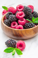 Wooden cup with fresh berries on white marble background