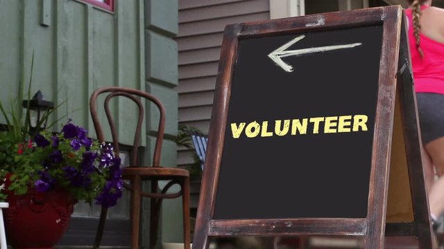 Woman walks past a sign that reads Volunteer and points to small business