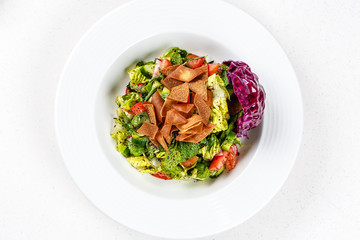 Fattoush or bread salad with pita croutons, fresh vegetables and herbs, on white plate on wooden table with sumac, lemon, olive oil gravy, easy and healthy authentic recipe