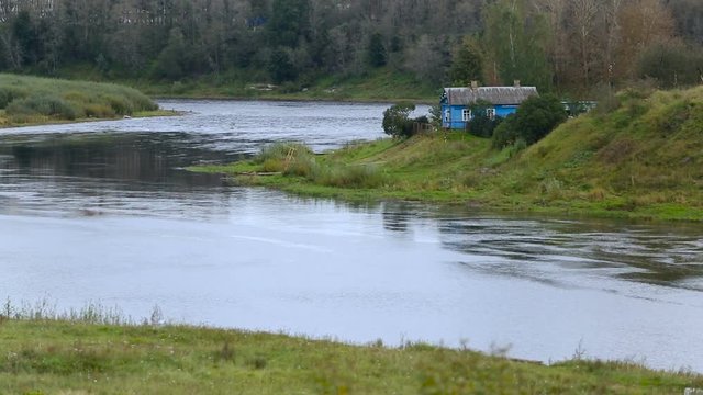 National Park. Small Country House on River Bank. Fast Water Streaming Down. Birch Forest on Background. Grass on Hill. Summer Day