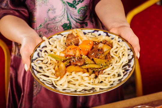 hand holding national dish of asian traditional food with noodles, meat and vegetables known as lagman