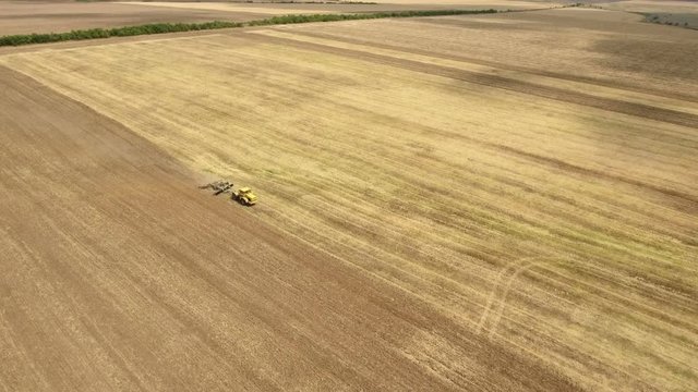 Wonderful view on a yellow tractor drawing a spike harrow to remove wheat straw and to do a  tillage from a bird`s eye perspective  in Eastern Europe in a sunny day. The tractor is shot in oblique way