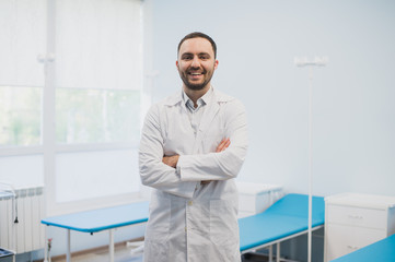 Portrait of a happy male doctor standing with arms crossed at medical office