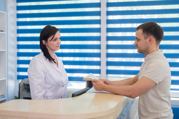 Mid adult female receptionist receiving card from patient in dentist clinic