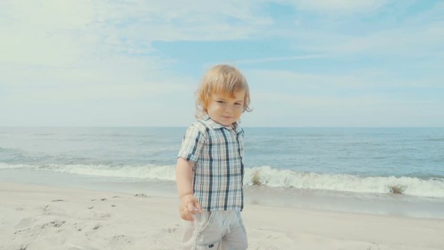 Adorable little 2 year old  boy in a shirt walking on the beach.  Child enjoys playing on the seashore . Slow Motion