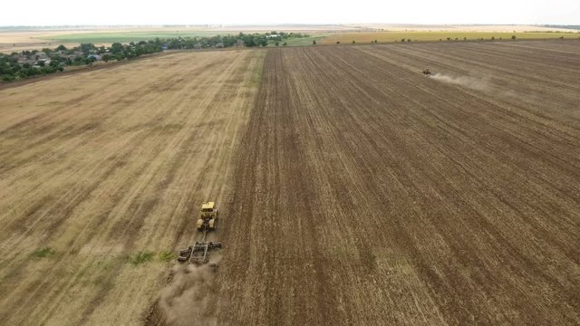 Gorgeous aerial shot of a big tractor drawing a spike and a disc harrows to remove wheat straw and to do a  tillage in Eastern Europe in a sunny day in summer. The drone is flying after the tractor