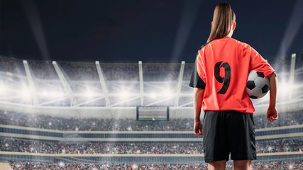 female soccer player standing with the ball against the crowded stadium at night