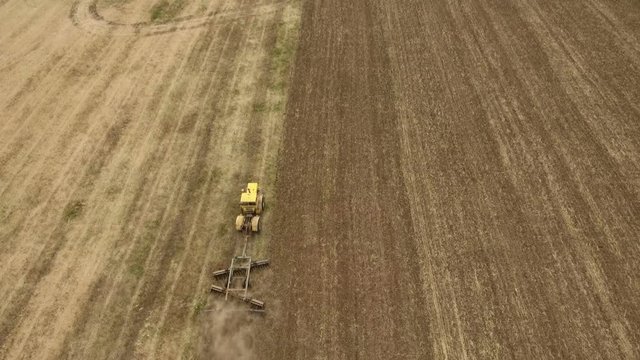 Amazing aerial shot of a big tractor drawing a spike and a disc harrows to remove wheat straw and to do a  tillage in Eastern Europe in a sunny day in summer. Thedrone is flying after the tractor