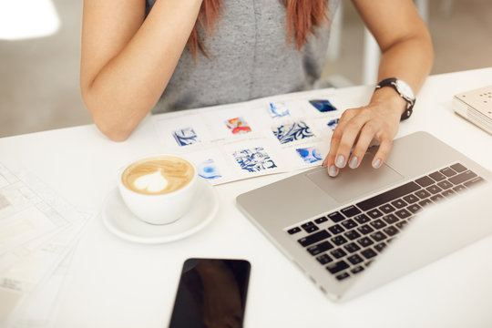 Close-up of fashion design student looking at fabric samples using laptop drinking coffee as usual
