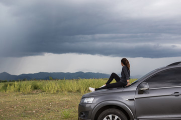 A woman sitting on a car skirt while having a storm.	