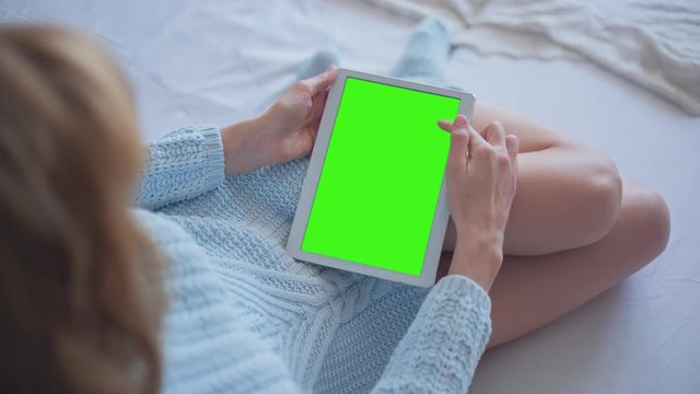 Young Woman in blue sweater laying on the bed uses Tablet PC with pre-keyed green screen. Few types of gestures - scrolling up and down, tapping, zoom in and out. Perfect for screen compositing