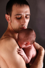 Fototapeta na wymiar an infant is held by his father with skin on skin contact, studio background 