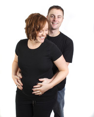  happy young couple with husbands hands on wife's belly laugh and smile in studio 