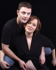  a young woman expecting a baby sits between the knees of her husband in studio 