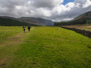 Fototapeta na wymiar Hikers on trail across meadow, Cumbria, England