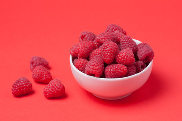 Bowl with fresh raspberries on a red background. Minimal concept. Copy space
