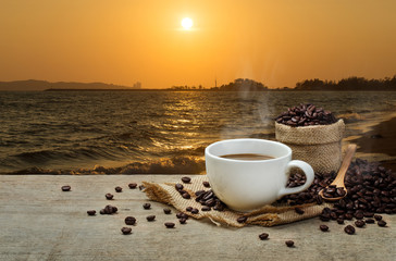 Hot Coffee cup with Coffee beans on the wooden table and the sea background