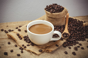 Hot Coffee cup with Coffee beans on the wooden table and the black background, vintage style color effect