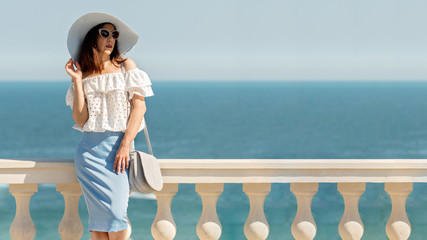 Young woman in a white blouse, blue pencil skirt and hat on a background of the sea horizon.