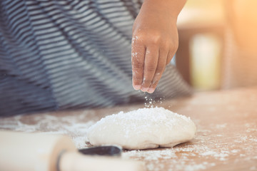 Little child girl hands prepares a dough for baking cookies in the kitchen in vintage color tone