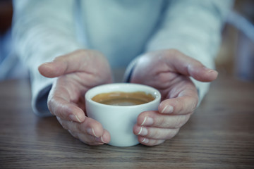 Female hands holding cups of coffee on rustic wooden table background - vintage style effect picture