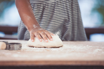 Little child girl hands prepares a dough for baking cookies in the kitchen in vintage color tone