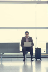 Asian Indian business man sitting on chair and using laptop while waiting his flight at airport.