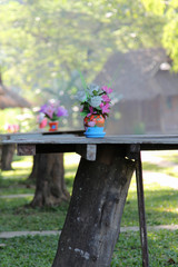 Rose artificial flower in the pot on wooden table in front of cottage resort.